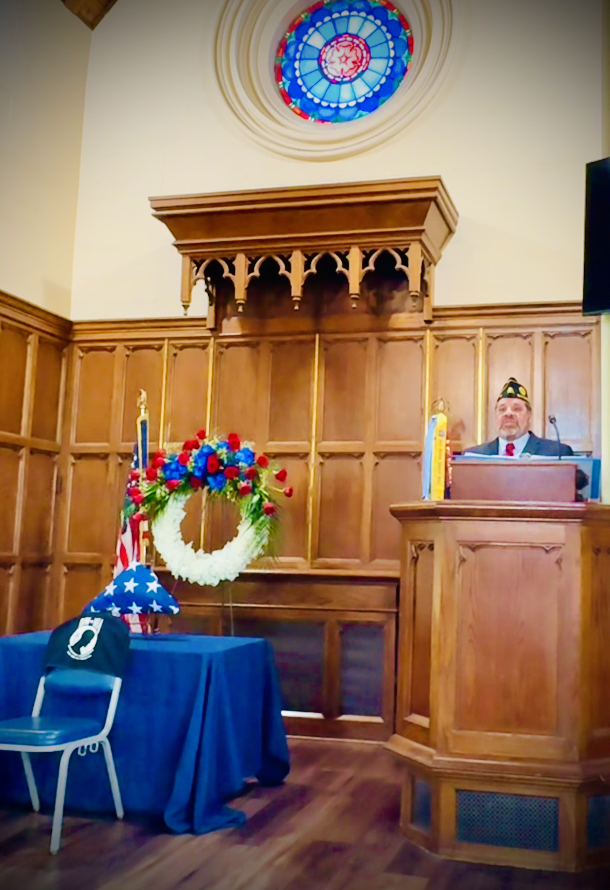 American Legion member speaking at Memorial Day ceremony with folded flag and memorial wreath