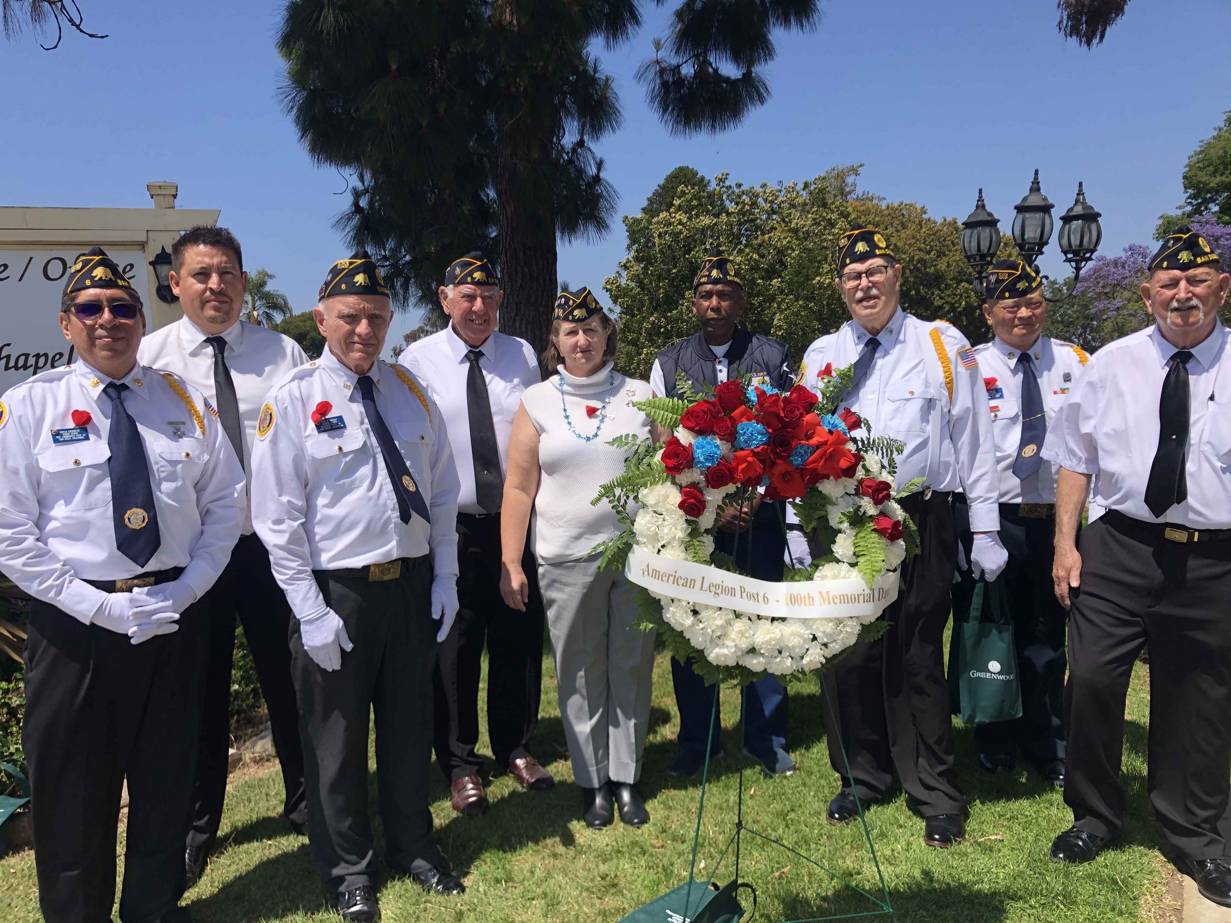 American Legion Post 6 members in formal white uniforms conducting outdoor Memorial Day wreath laying ceremony with patriotic red, white, and blue wreath