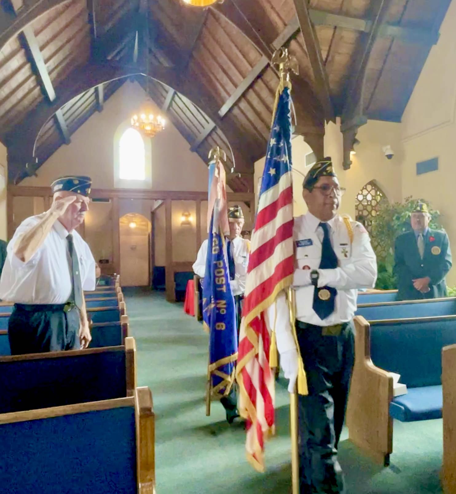 Memorial Day flag ceremony inside chapel with American Legion honor guard and stained glass windows